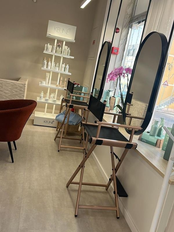Posto de atendimento com espelho em arco, prateleiras brancas de produtos e uma orquídea.