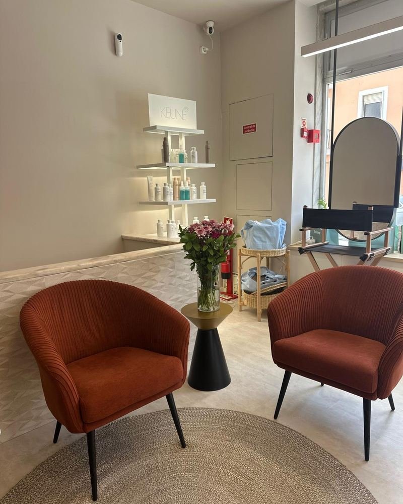 Zona de receção e espera do Amalfi Beauty Hair, com dois cadeirões em tom terracota, mesa de apoio com flores e estantes iluminadas em fundo.